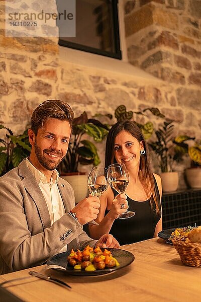 Lifestyle  ein hübsches  verliebtes junges Paar in einem Restaurant  das mit einem Glas Wein anstößt  um den Valentinstag zu feiern  vertikales Foto