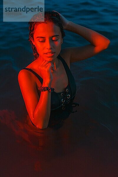 Eine junge kaukasische Brünette badet nachts im Meer mit einem beleuchteten roten Licht