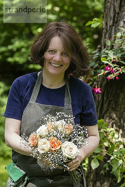 Gärtnerin mit Blumenstrauß und Schürze im Garten  gardener with bouquet of flowers and apron in a garden