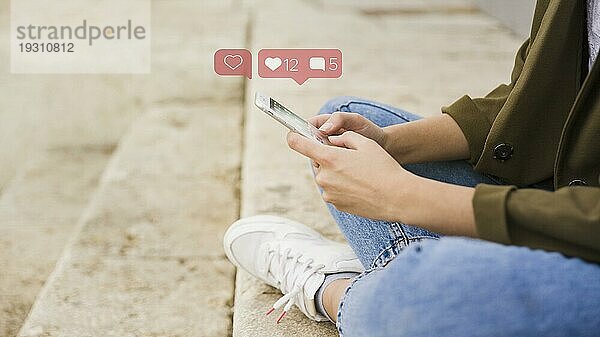 Nahaufnahme einer Frau  die auf einer Treppe sitzt und eine mobile Social Media App benutzt