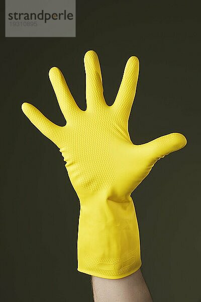 Hand mit einem gelben Gummihandschuh zum Schutz