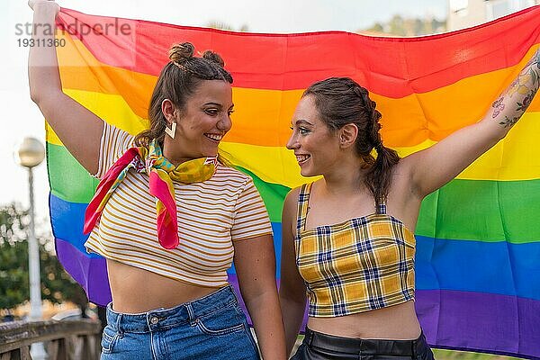 Eine Nahaufnahme von zwei jungen kaukasischen Frauen halten hoch LGBT Stolz Flagge im Freien