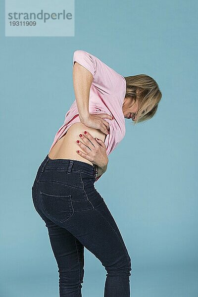 Unzufriedene Frau  die an Schmerzen im unteren Rückenbereich leidet  blaür Hintergrund