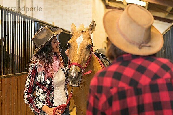 Zwei Cowgirl Frauen  die ein Pferd streicheln  mit südamerikanischem Outfit  Lebensstil von zwei Frauen  die in einem Stall arbeiten