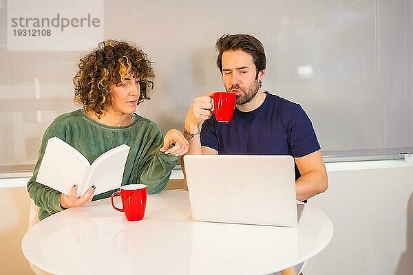 Lifestyle  ein junges kaukasisches Paar im Schlafanzug beim Frühstück in der Küche  ein Mädchen  das ein Buch liest  und ein Junge  der E Mails am Computer liest