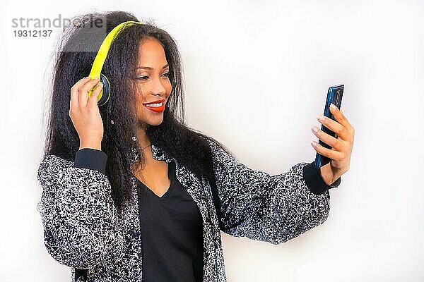 Vertikale Nahaufnahme einer fröhlich lächelnden hispanischen Frau  die mit Kopfhörern Musik genießt  vor weißem Hintergrund