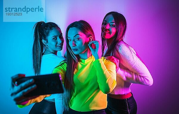 Lebensstil von Freunden  die in einer Disco mit blauen und rosa Neonlichtern feiern und Spaß daran haben  ein Foto mit dem Handy für soziale Netzwerke zu machen