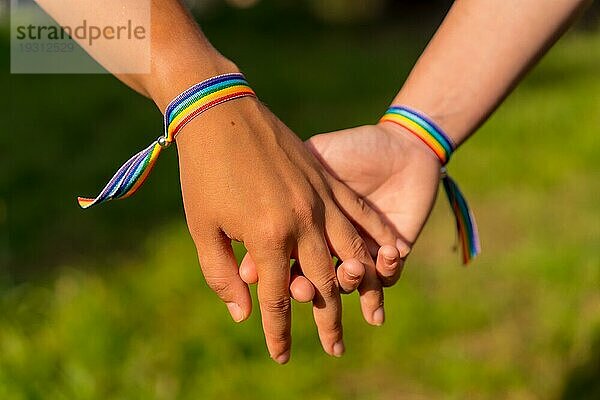 Eine Nahaufnahme von zwei jungen kaukasischen Frauen  die sich mit LGBT Stolz Armbändern im Freien an den Händen halten