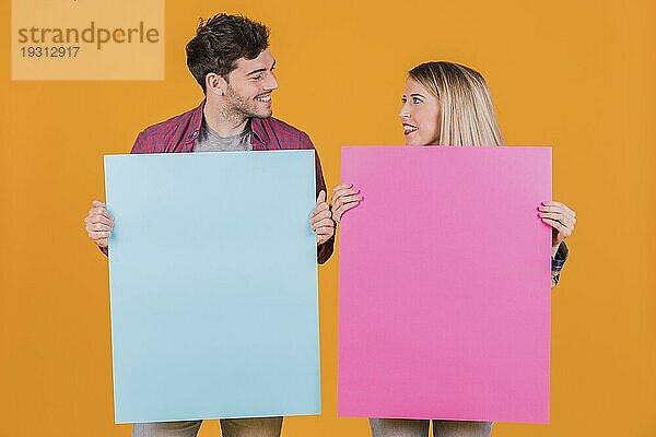 Portrait junges Paar hält blaues rosa Plakat vor orangem Hintergrund