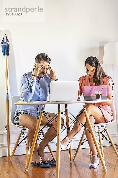 Ein Paar  das zu Hause telearbeitet  Schwierigkeiten der neuen Arbeitsnormalität  ein kaukasisches Paar  das an einem Tisch mit Computern im Wohnzimmer seines Hauses arbeitet