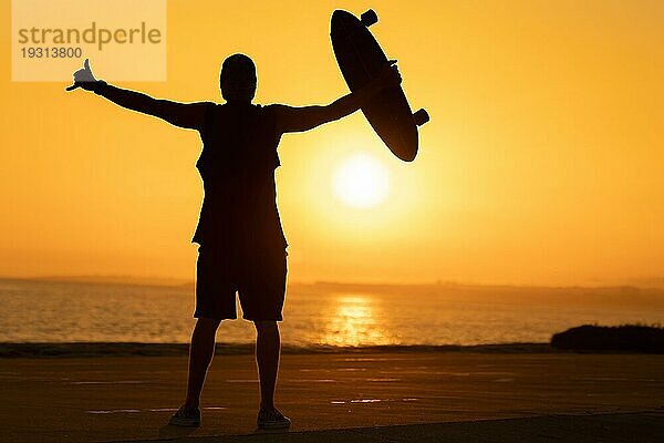 Silhouette eines Mannes  der einen Shaka zeigt und ein Skateboard bei Sonnenuntergang hält. Mittlere Aufnahme