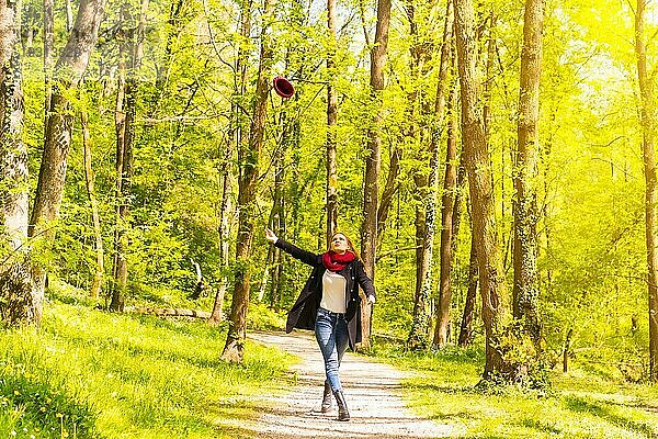 Lateinamerikanisches Mädchen mit schwarzer Jacke  Schal und roter Wollmütze in einem herbstlichen Park  das den Hut wirft  während es fröhlich spazieren geht