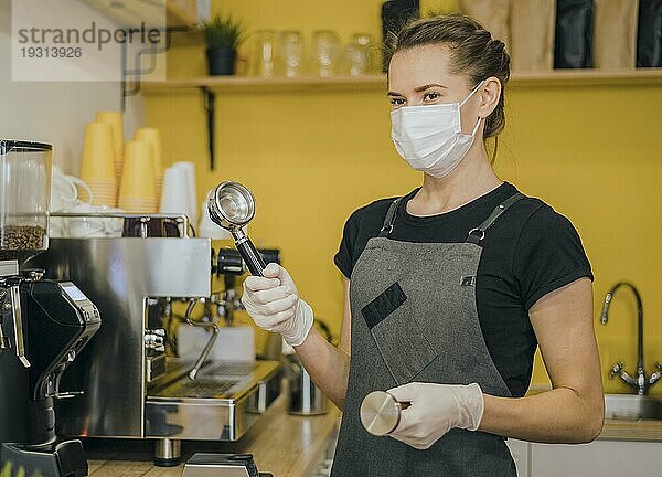 Seitenansicht einer weiblichen Barista mit medizinischer Maske  die eine Kaffeemaschine vorbereitet