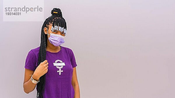 Internationaler Frauentag im Jahr der Coronaviruspandemie Covid 19. Dominikanische Frau mit feministischem lila Hemd und Gesichtsmaske