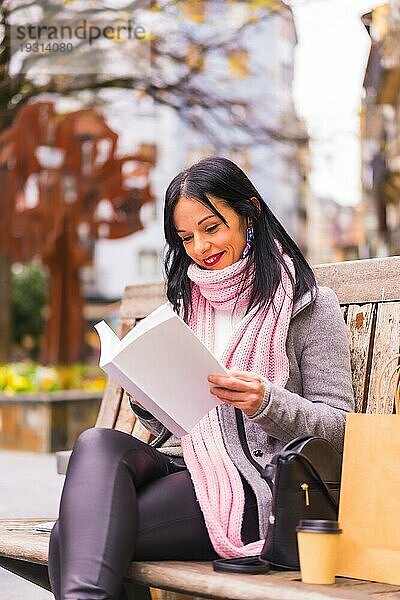 Lifestyle  kaukasisches brünettes Mädchen liest ein Buch in einem Park  lächelnd auf einer Bank sitzend