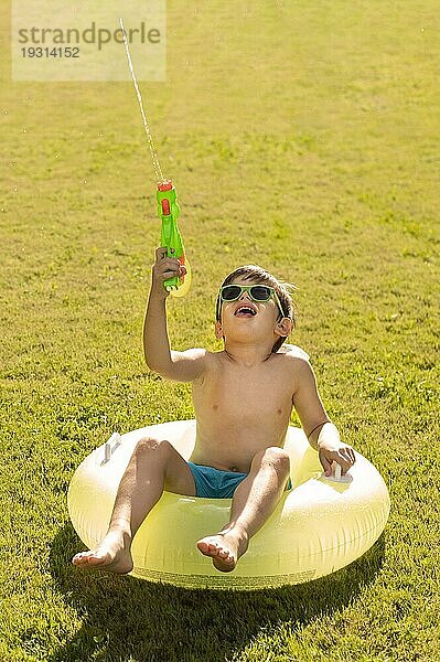 Junge mit Hut und Sonnenbrille spielt mit Wasserpistole