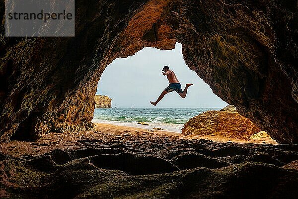 Ein Mann springt in die natürliche Höhle an der Algarve am Strand von Praia da Coelha  Albufeira. Portugal