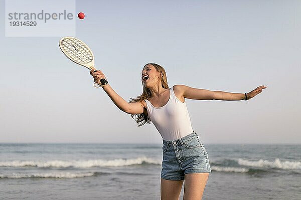 Glückliches Mädchen spielt Tennis am Meer