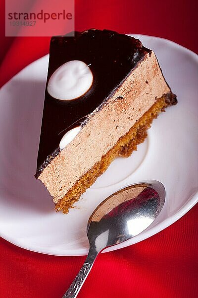 Schokoladenkuchen mit Löffel auf dem Teller auf rotem Seidenhintergrund. Unscharfer Fokus