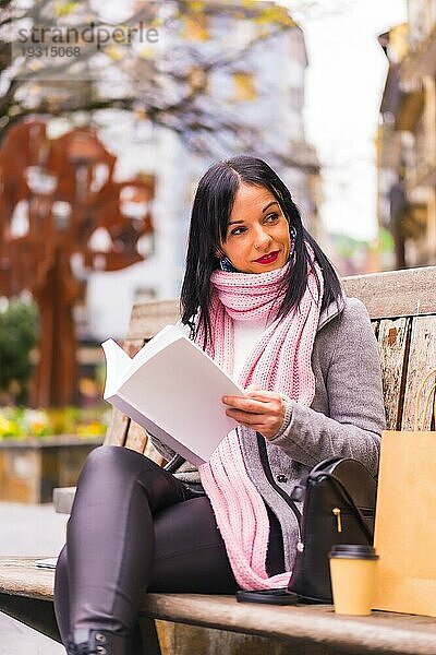 Lifestyle  kaukasisches brünettes Mädchen liest ein Buch in einem Park  lächelnd auf einer Bank sitzend