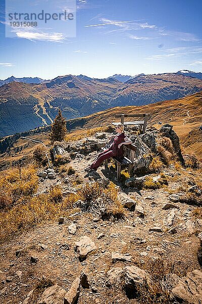 Wanders Frau auf Bank am Gipfelkreuz in felsiger Gebiergslandschaft im Herbst  Hirschkarspitze  Alpen  Österreich  Europa