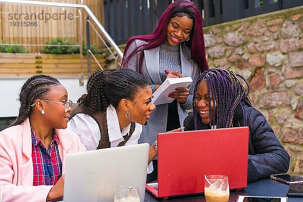 Junge und alternative Geschäftsfrauen schwarzer Ethnie. In einer Teamwork Sitzung  in einer Cafeteria mit Computern und Notizen