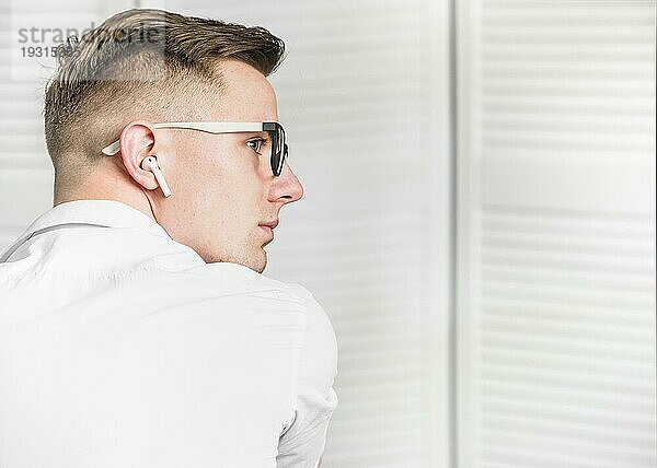 Seitenansicht junger Mann mit weißem drahtlosen Kopfhörer und Brille  der wegschaut