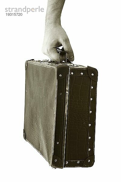 Sepia getöntes Foto einer Hand  die einen alten Koffer hält. Kurze Schärfentiefe  die Schärfe liegt in der Hand