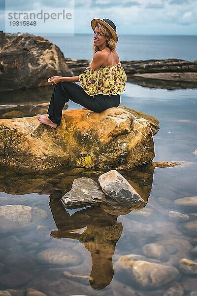 Mädchen in geblümter Bluse  schwarzen Shorts und Strohhut in einer Naturlandschaft am Meer