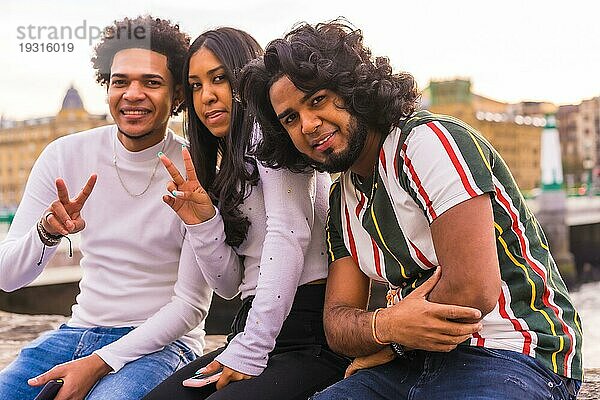 Lifestyle  Porträt von drei schwarzen Freunden  die Spaß in der Stadt mit dem Sonnenuntergang im Hintergrund  Abnehmen und Millennial in der Stadt. Afro Haar Junge  Brünette Junge mit langen Haaren und Brünette Mädchen