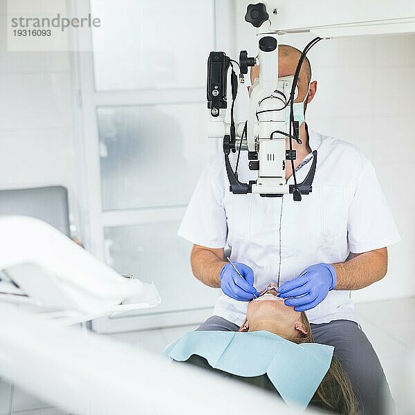 Professioneller Zahnarzt bei der Untersuchung eines Patienten mit einem Dentalmikroskop