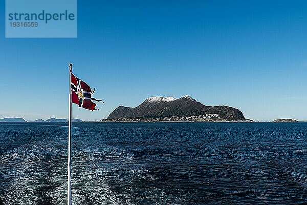 Norwegische Postflagge  gehisst am Mast eines Postschiffs  das im Wind weht  mit offenem Meer und Bergen an einem sonnigen Wintertag