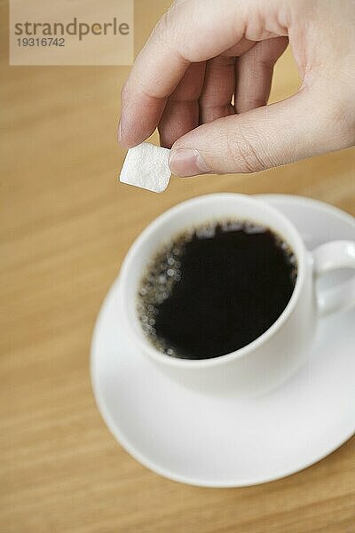 Eine Hand gibt Zucker in eine Tasse Kaffee. Kurze Tiefenschärfe