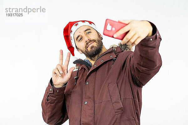 Sehr glücklicher junger kaukasischer Mann mit roter Weihnachtsmütze  der ein Selfie auf einem weißen Hintergrund macht