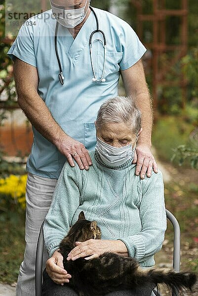 Vorderansicht einer älteren Frau mit medizinischer Maske  die von einem Pfleger gepflegt wird