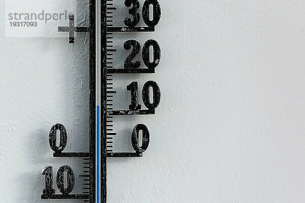 Klassisches analoges Thermometer  das an einer weißen Wand hängt und eine Temperatur von zwölf Grad Celsius anzeigt