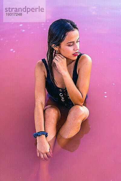 Posing einer jungen brünetten Kaukasierin im Sommerurlaub in der rosa Lagune von Torrevieja  die mit verführerischem Blick im Wasser sitzt  Alicante. Spanien