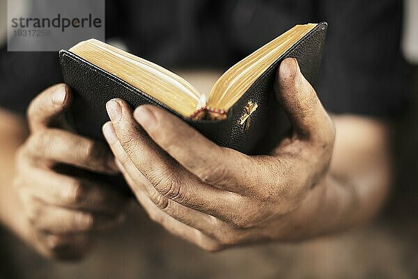 Schmutzige Hände halten eine alte Bibel. Sehr geringe Tiefenschärfe