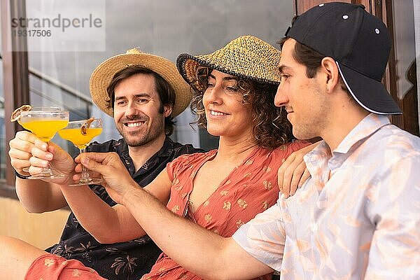 Lässige drei kaukasische Freunde stoßen mit Cocktails entspannt auf einer Terrasse sitzend an
