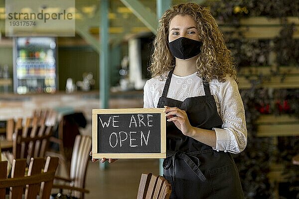 Frau mit Maske hält Kreidetafel mit offenem Schild