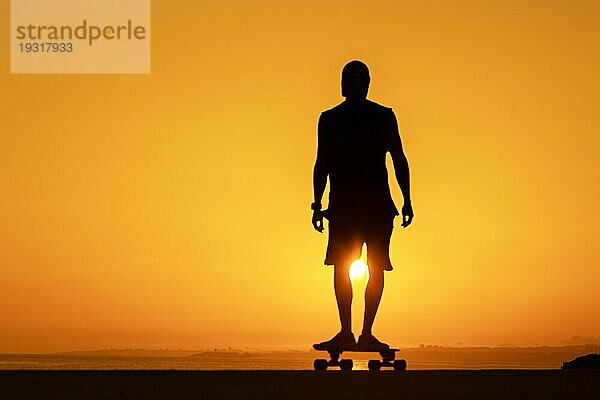 Silhouette eines Mannes  der bei Sonnenuntergang auf einem Skateboard steht. Mittlere Aufnahme