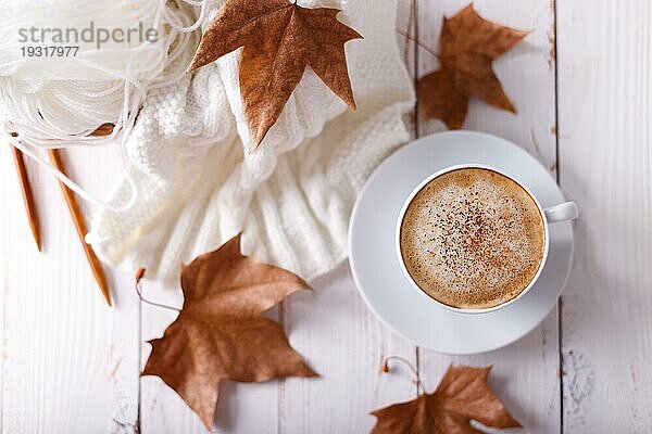 Heißer Kaffee Cappuccino  gestrickte Decke und Herbstblätter auf altem Holzhintergrund. Saisonale entspannen Konzept