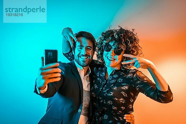 Party Lifestyle  ein verliebtes kaukasisches Paar macht ein Selfie auf einer Party mit orangefarbenen und blauen Lichtern  am Valentinstag