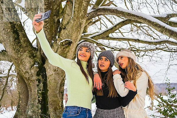 Winter Lifestyle  drei schöne kaukasische Freunde nehmen ein Selfie mit dem Telefon im Schnee unter einem Baum  Urlaub in der Natur