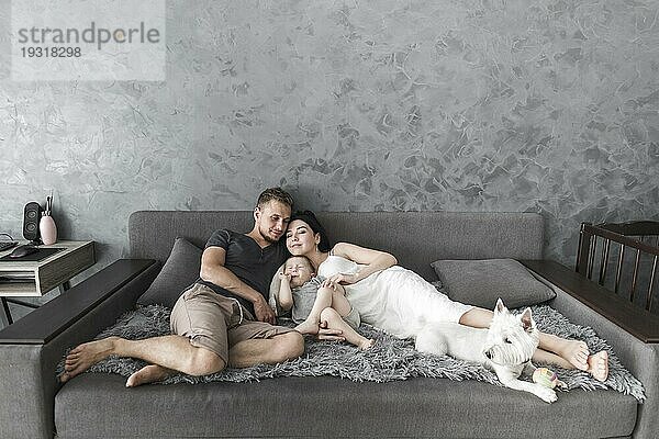 Junges Paar entspannt auf dem Sofa mit ihrem Sohn weißen Hund