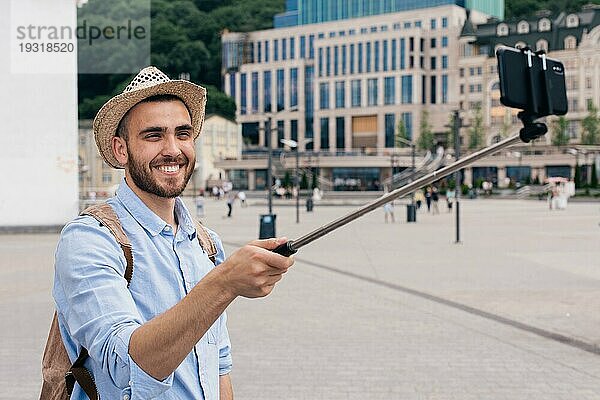 Porträt glücklicher junger Mann  der einen Rucksack trägt und ein Selfie mit seinem Smartphone macht