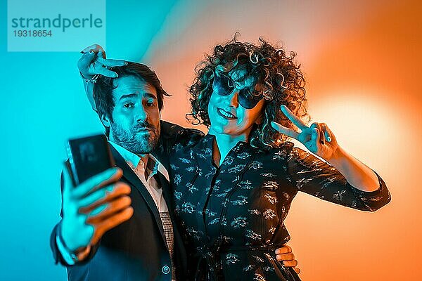 Party Lifestyle  ein verliebtes kaukasisches Paar macht ein Selfie auf einer Party mit orangefarbenen und blauen Lichtern  am Valentinstag