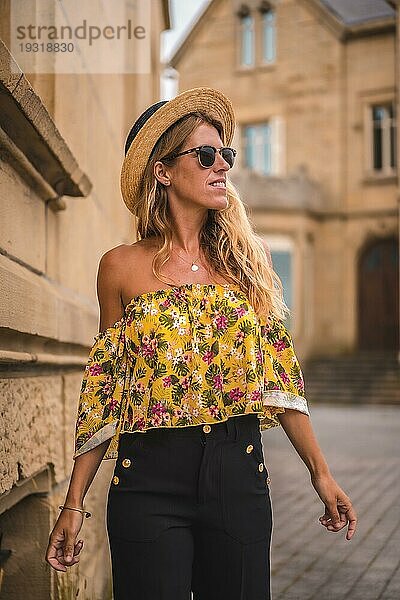 Blonde Frau lächelnd mit einem gelben Vintage Outfit mit einem Hut besuchen ein Schloss