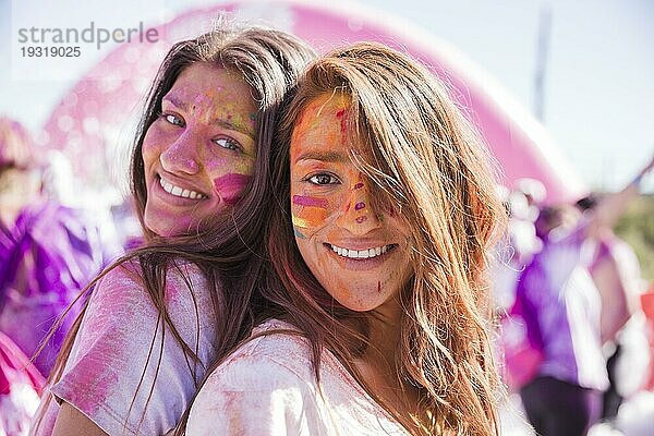 Lächelnde junge Frauen mit Holi Farbe ihr Gesicht stehen wieder zurück