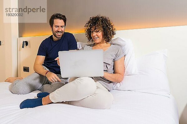 Lifestyle  ein heterosexuelles kaukasisches Paar im Schlafanzug auf dem Bett  das eine Online Reservierung auf dem Computer betrachtet